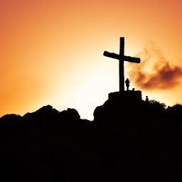 human standing beside crucifix statue on mountain